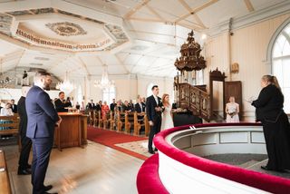 Alttarin suunnalta kuvattu näkymä kirkkoon, jossa hääpari on vihittävänä häävieraiden seisoessa katsomassa toimitusta.